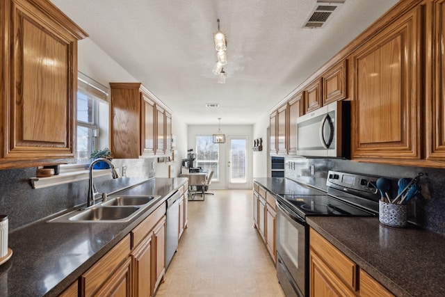 kitchen featuring stainless steel appliances, a sink, visible vents, brown cabinetry, and dark countertops