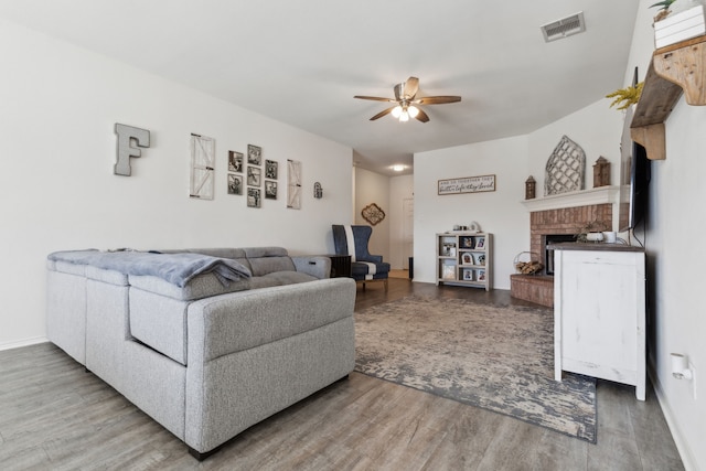 living room featuring a brick fireplace, ceiling fan, visible vents, and wood finished floors