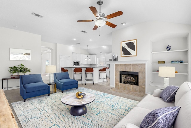 living area with vaulted ceiling, arched walkways, visible vents, and a tile fireplace