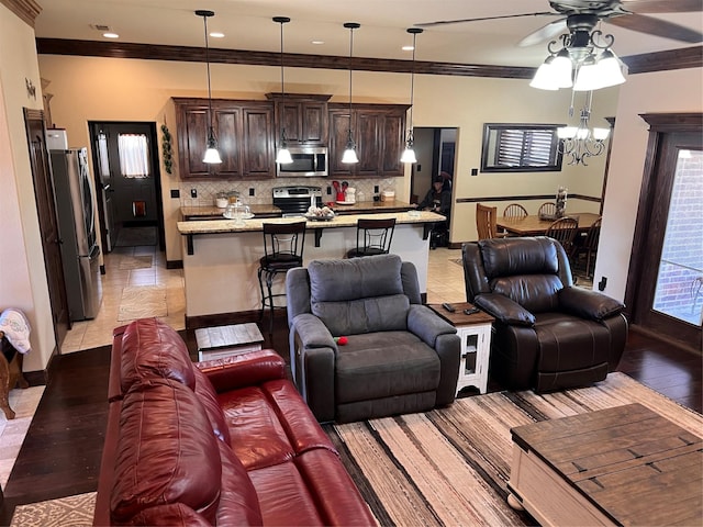 living room featuring ceiling fan with notable chandelier, ornamental molding, light wood-style flooring, and baseboards