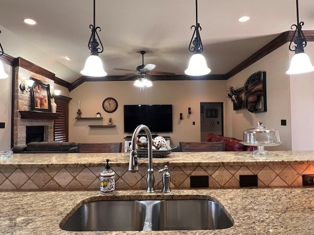 kitchen with ornamental molding, open floor plan, a sink, and a stone fireplace