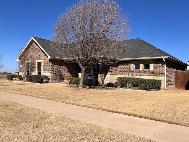 single story home with a shingled roof, a front yard, and brick siding