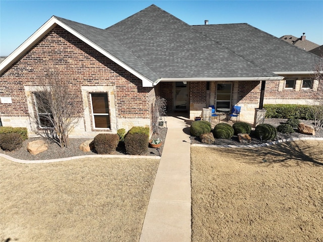 view of front of house featuring covered porch, brick siding, and roof with shingles