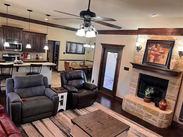 living room featuring ceiling fan, a stone fireplace, light wood-style flooring, baseboards, and ornamental molding