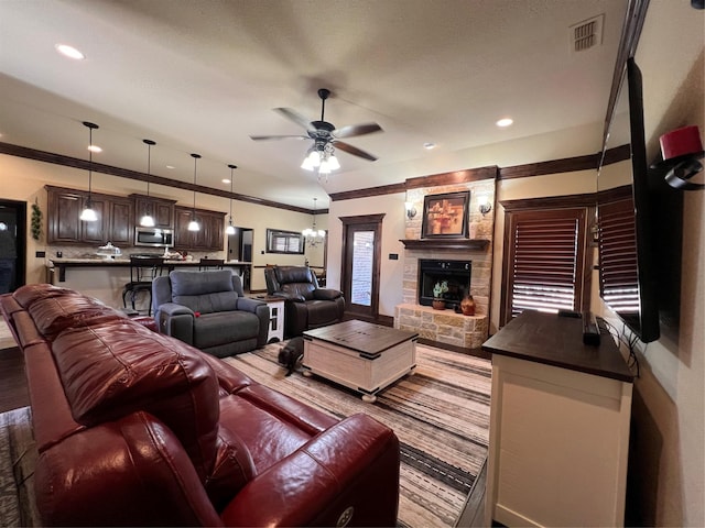 living area with crown molding, recessed lighting, visible vents, a ceiling fan, and a stone fireplace