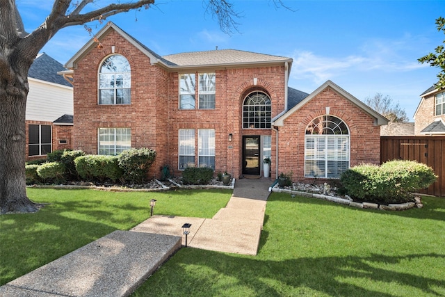 view of front of house with roof with shingles, a front yard, fence, and brick siding