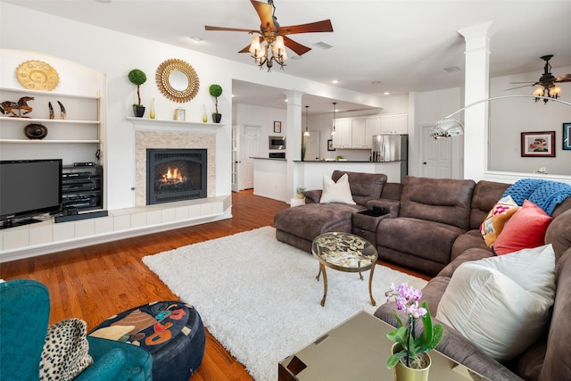 living area with decorative columns, visible vents, a tiled fireplace, ceiling fan, and wood finished floors