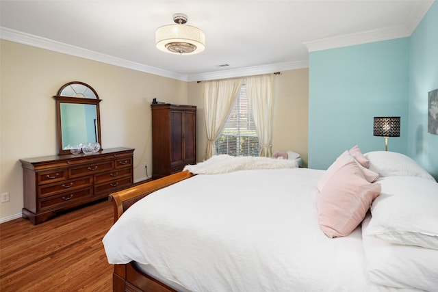 bedroom featuring visible vents, crown molding, baseboards, and wood finished floors