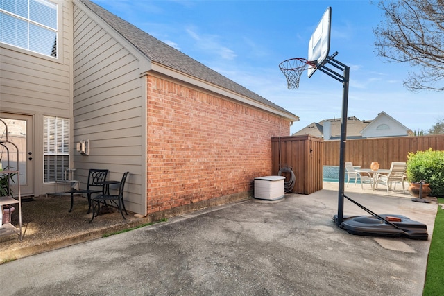 view of side of property with a shingled roof, a patio area, brick siding, and fence