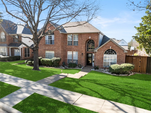 traditional-style house with brick siding, a front lawn, a shingled roof, and fence