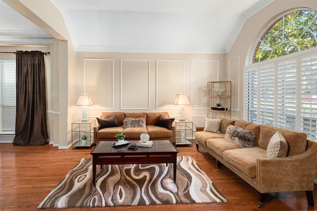 living area featuring lofted ceiling, ornamental molding, wood finished floors, and a decorative wall