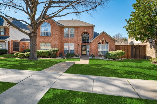 view of front facade featuring a shingled roof, a front yard, brick siding, and fence