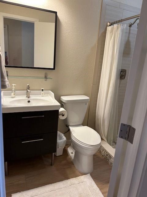 bathroom featuring a textured wall, toilet, wood finished floors, vanity, and a shower stall