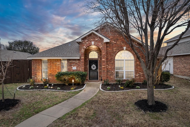 view of front of house with a yard, brick siding, a shingled roof, and fence