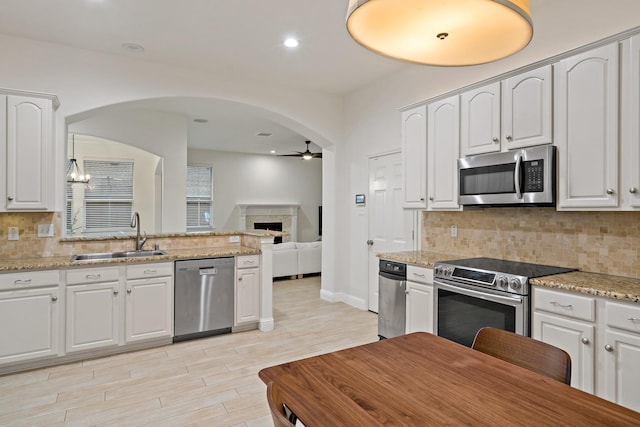 kitchen with ceiling fan, stainless steel appliances, a fireplace, a sink, and white cabinetry