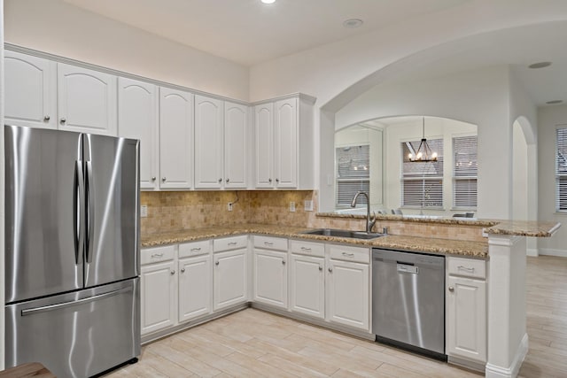 kitchen featuring light wood finished floors, appliances with stainless steel finishes, white cabinets, a sink, and a peninsula