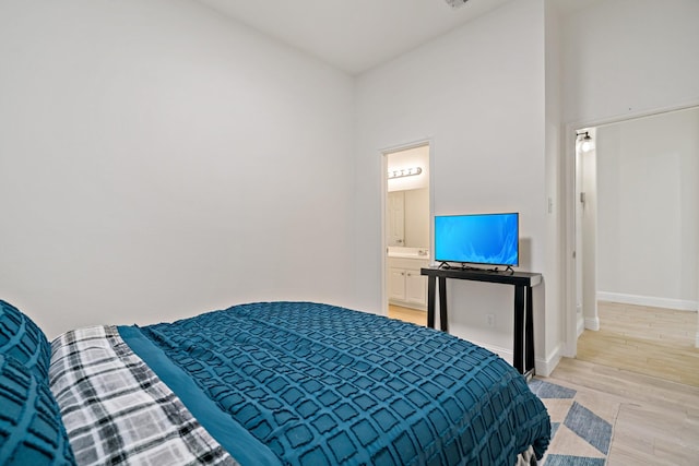 bedroom with light wood-style flooring, baseboards, and connected bathroom