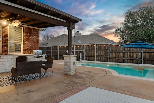 pool at dusk featuring an outdoor kitchen, fence, grilling area, and a fenced in pool