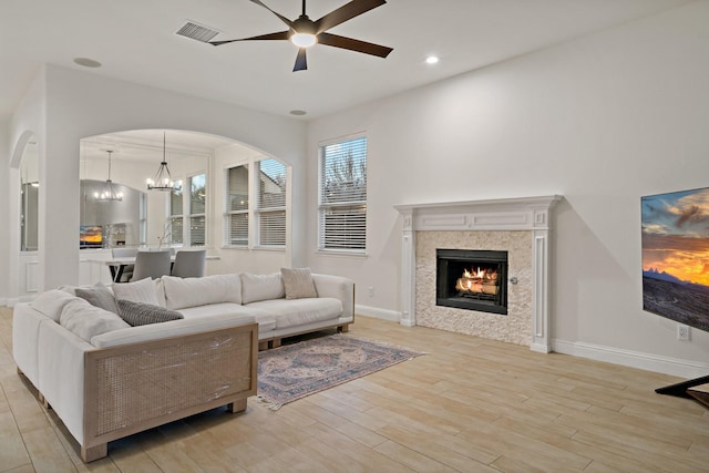 living area with visible vents, arched walkways, a tile fireplace, wood finished floors, and ceiling fan with notable chandelier