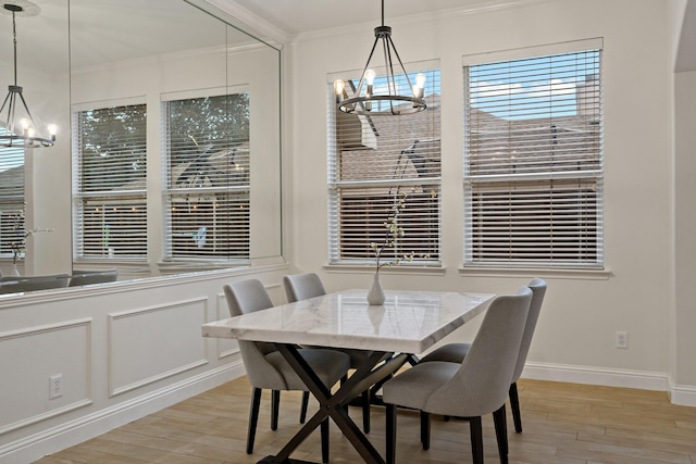 dining room with light wood finished floors, a chandelier, a decorative wall, and ornamental molding