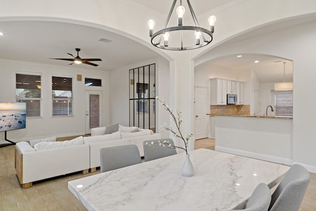 dining area with arched walkways, ceiling fan with notable chandelier, light wood-type flooring, and visible vents