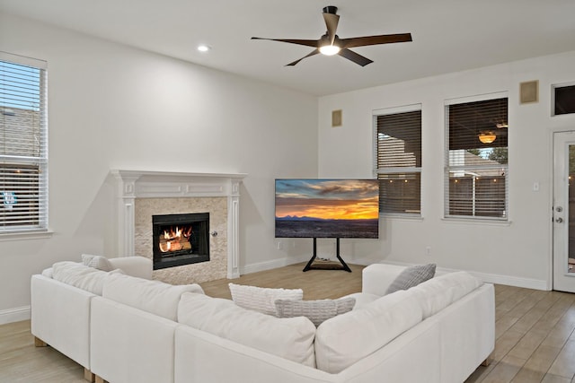 living area featuring baseboards, ceiling fan, a tile fireplace, and light wood-style floors