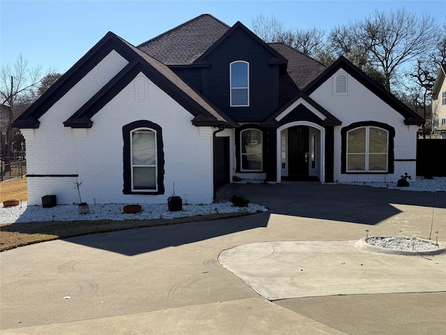 french country home with driveway, brick siding, and roof with shingles