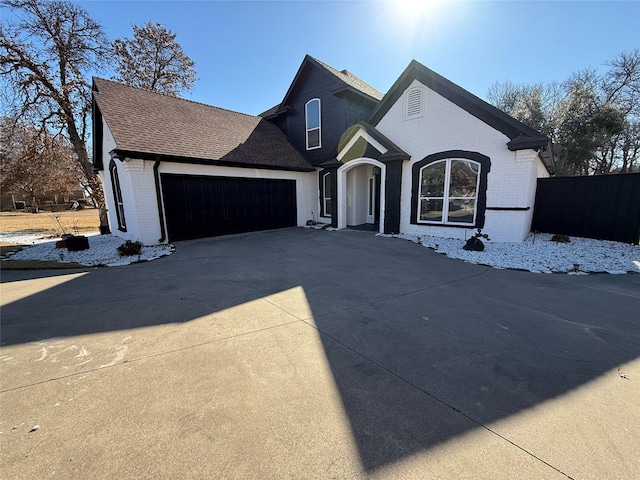 view of front facade with an attached garage, brick siding, fence, driveway, and roof with shingles