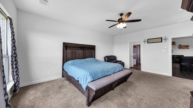 carpeted bedroom with ensuite bath, baseboards, visible vents, and ceiling fan