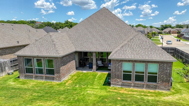 rear view of property with a yard, brick siding, a shingled roof, and fence