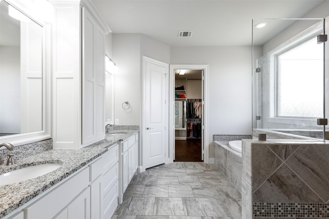 bathroom featuring double vanity, a relaxing tiled tub, a sink, and visible vents