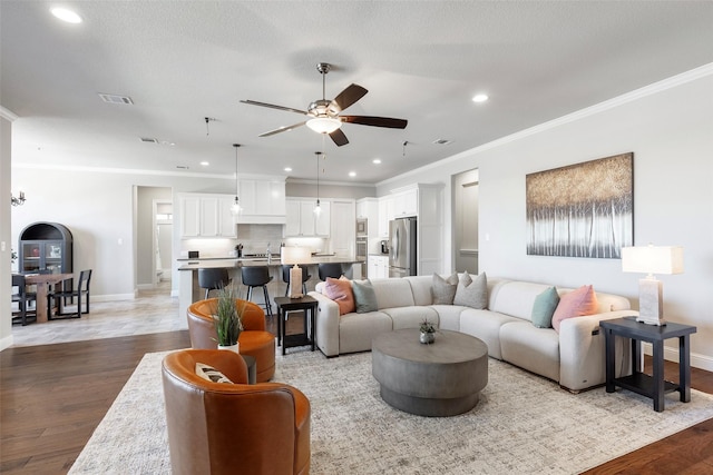 living room with light wood finished floors, visible vents, ornamental molding, a ceiling fan, and baseboards