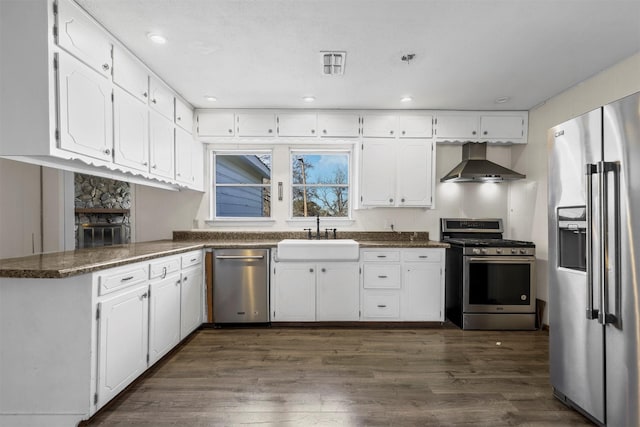 kitchen featuring wall chimney range hood, appliances with stainless steel finishes, white cabinets, and a sink