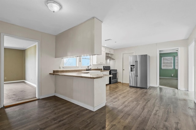 kitchen featuring appliances with stainless steel finishes, dark wood-style flooring, wall chimney range hood, and a peninsula