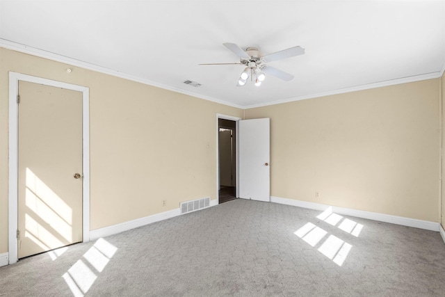 carpeted spare room featuring a ceiling fan, baseboards, visible vents, and crown molding