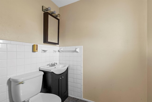 half bathroom with toilet, wainscoting, vanity, and tile walls