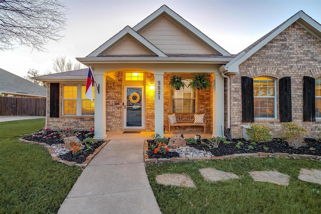 view of front of home featuring a front lawn, fence, covered porch, and brick siding