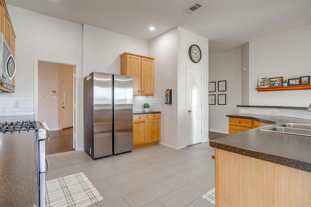 kitchen with a sink, stainless steel appliances, dark countertops, and visible vents