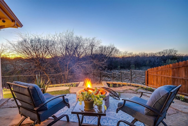 patio terrace at dusk featuring an outdoor fire pit and fence