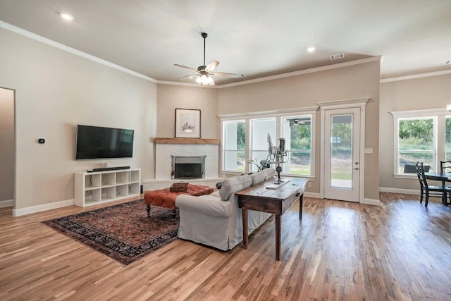 living area with a fireplace, baseboards, wood finished floors, and ornamental molding