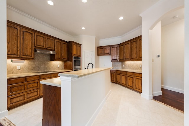 kitchen with a center island with sink, ornamental molding, black electric cooktop, light countertops, and under cabinet range hood