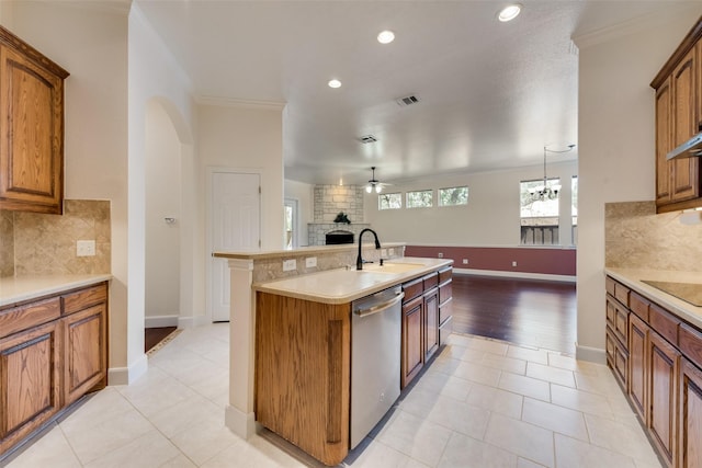 kitchen featuring a large fireplace, brown cabinetry, dishwasher, an island with sink, and a sink