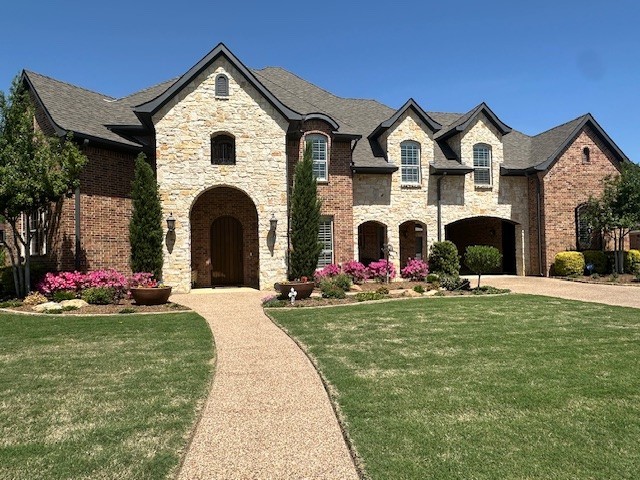 french country inspired facade featuring driveway, a front yard, and stone siding