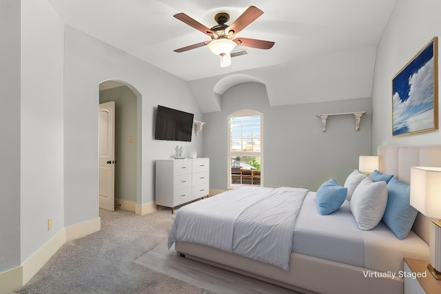 bedroom with baseboards, arched walkways, ceiling fan, vaulted ceiling, and light carpet