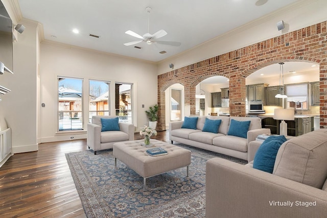 living room with dark wood-type flooring, ceiling fan, arched walkways, and brick wall
