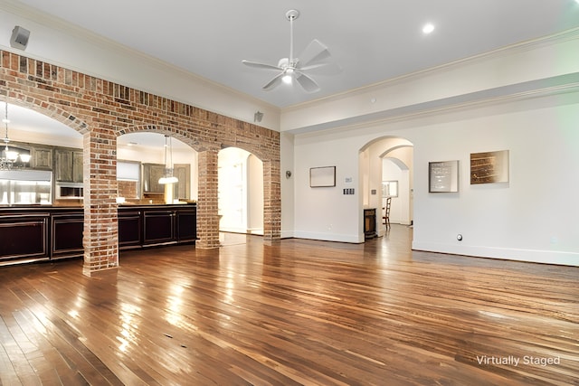 unfurnished living room featuring arched walkways, dark wood-style floors, a ceiling fan, and crown molding