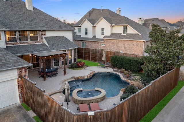 pool at dusk featuring a patio, a fenced backyard, and a pool with connected hot tub