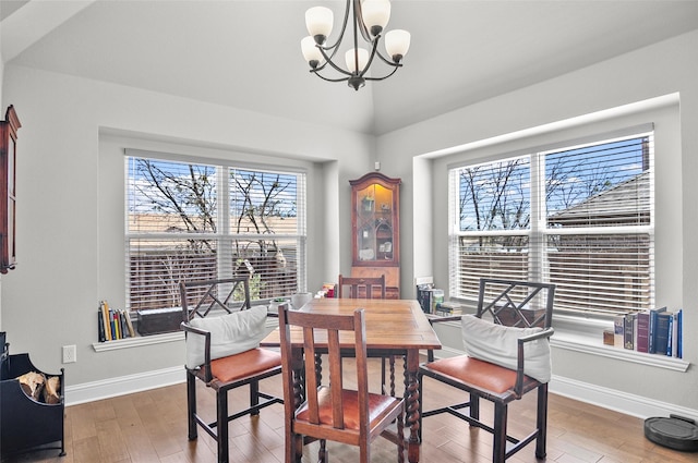 dining space with lofted ceiling, baseboards, an inviting chandelier, and wood finished floors