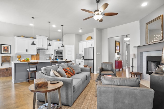 living area with ceiling fan, recessed lighting, a brick fireplace, and light wood-style floors