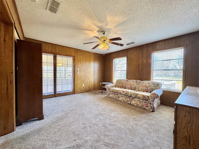 unfurnished room with carpet, visible vents, ceiling fan, wooden walls, and a textured ceiling